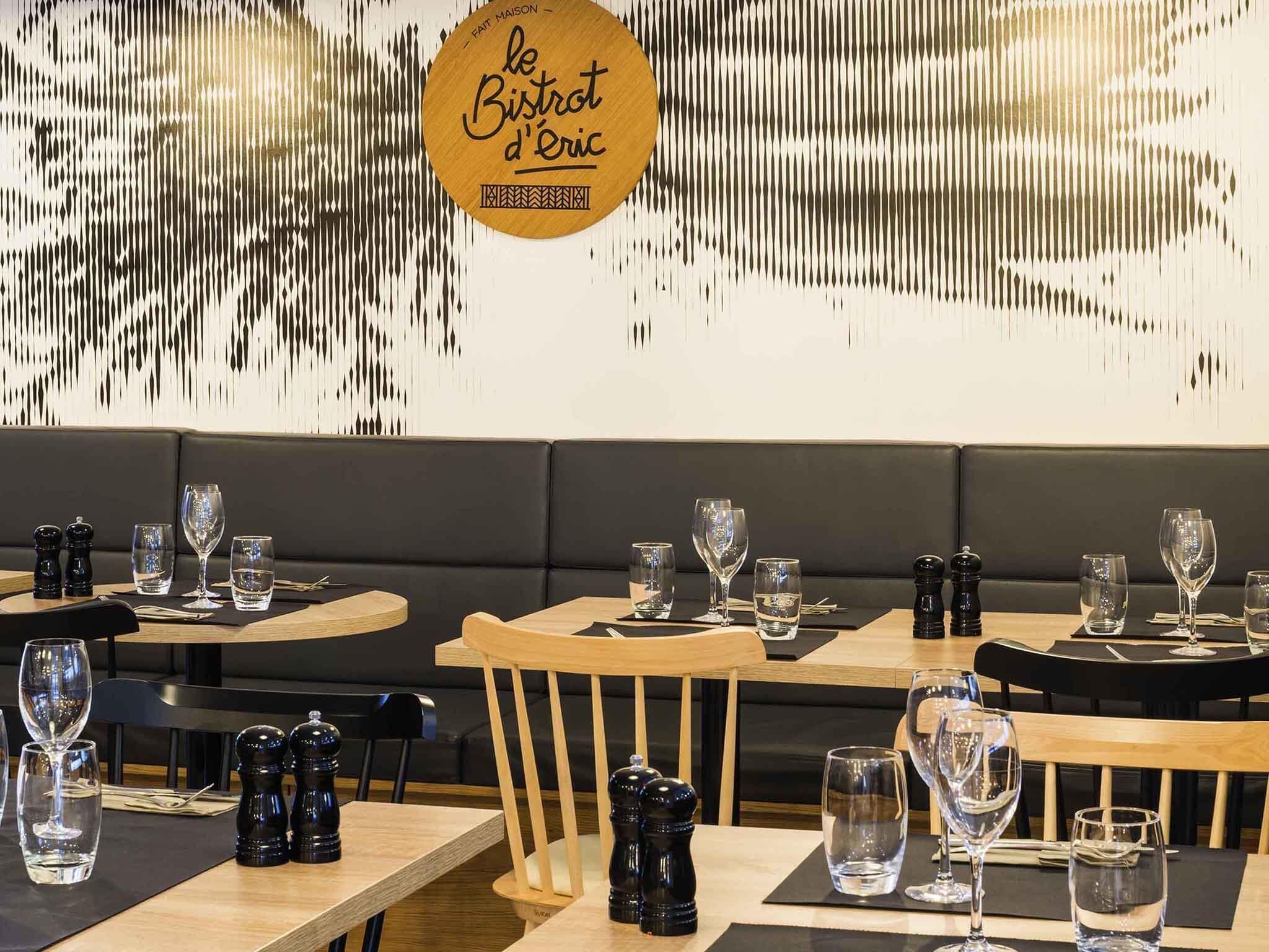 Een restaurantinterieur met houten tafels, zwart beklede zitplaatsen en een decoratieve muur met een logo.