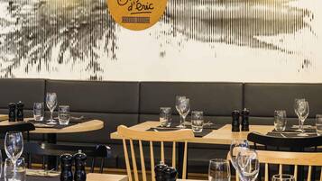 Een restaurantinterieur met houten tafels, zwart beklede zitplaatsen en een decoratieve muur met een logo.