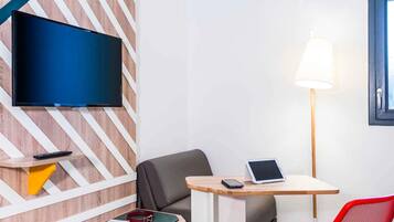 Een moderne hotelkamer met een flatscreen televisie aan een houten wand, een bureau met een lamp, een stoel, en een rode stoel.