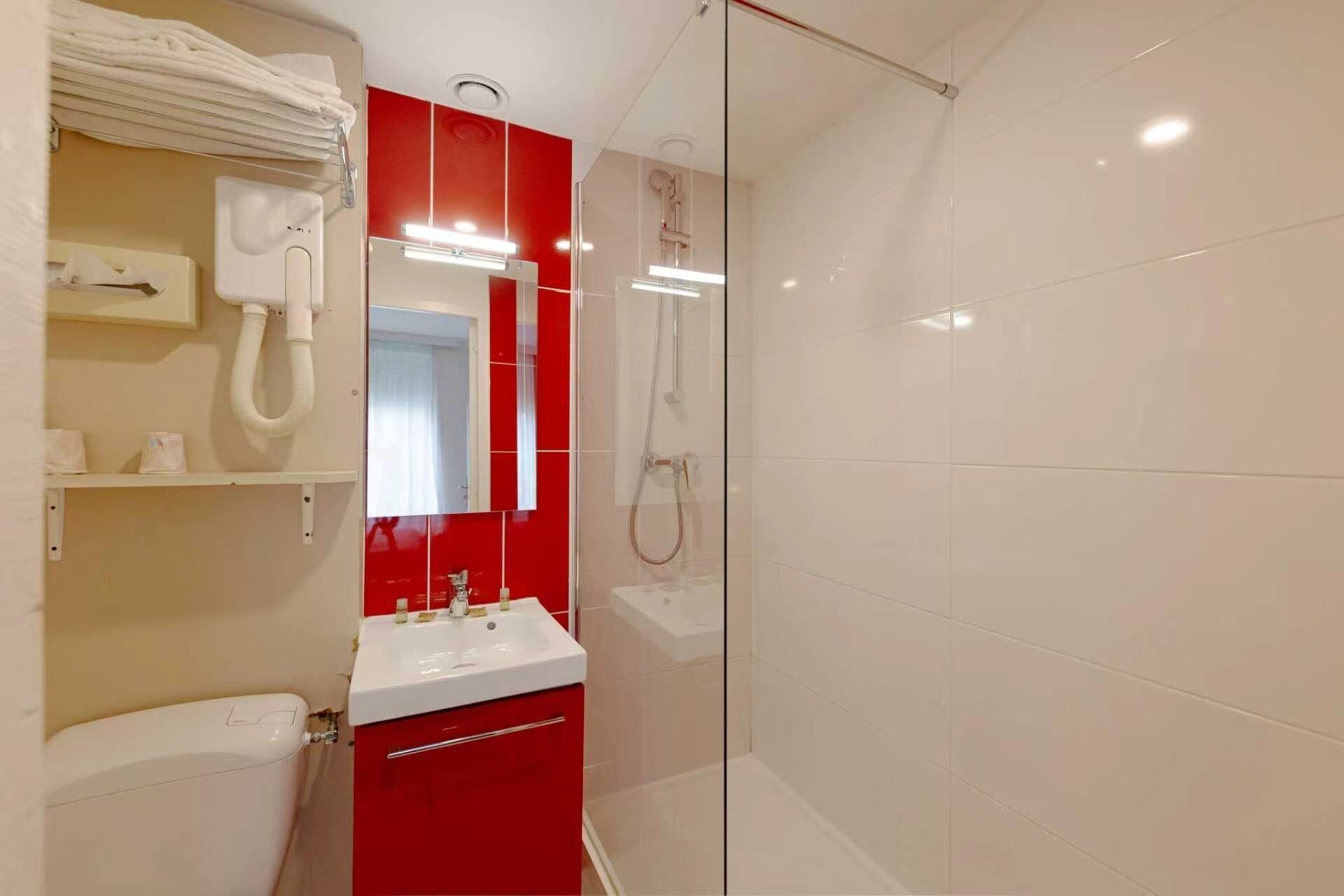 A bathroom with a glass shower enclosure, a white sink, and red cabinetry.