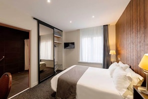 A hotel room with a bed, a TV, a desk with a lamp, a shower area, and a wardrobe. - Hôtel Metropol (Calais)