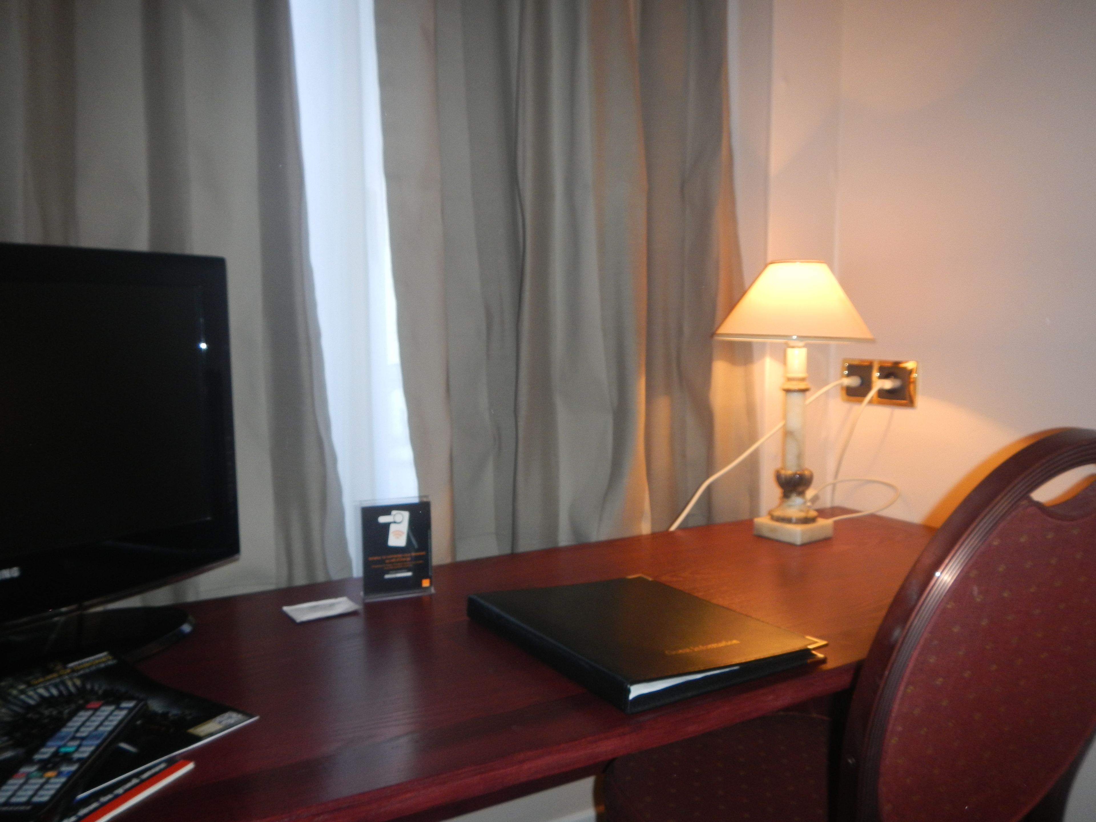 A hotel room with a desk, a television, a lamp, and a chair.