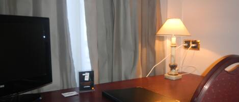 A hotel room with a desk, a television, a lamp, and a chair.