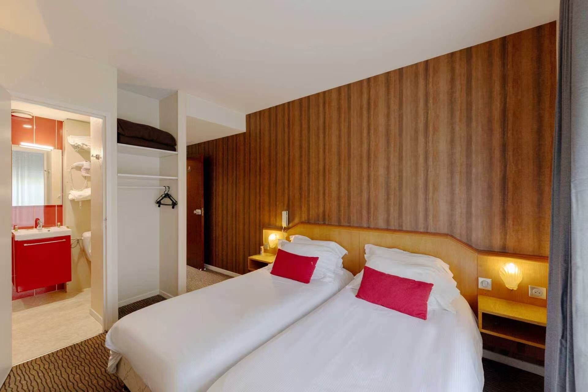 Une chambre d’hôtel avec deux lits, une salle de bain rouge et un lambris en bois sur le mur.