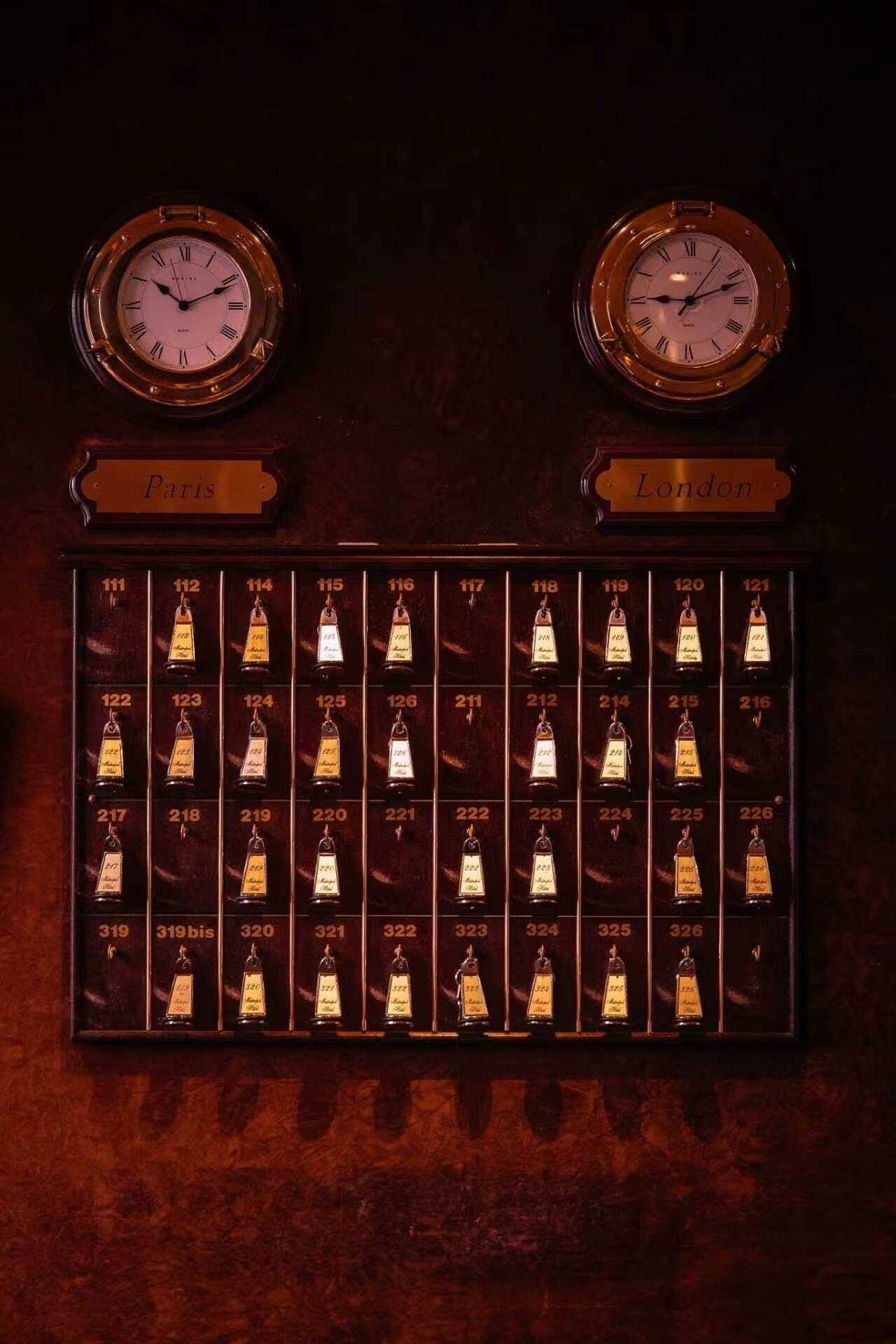 Una pantalla montada en la pared con dos relojes etiquetados 'París' y 'Londres', y una cuadrícula de botellas numeradas.