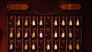 Una pantalla montada en la pared con dos relojes etiquetados 'París' y 'Londres', y una cuadrícula de botellas numeradas.