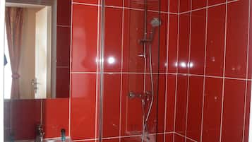 Un baño con baldosas rojas, una ducha con mampara de vidrio y un lavabo blanco.