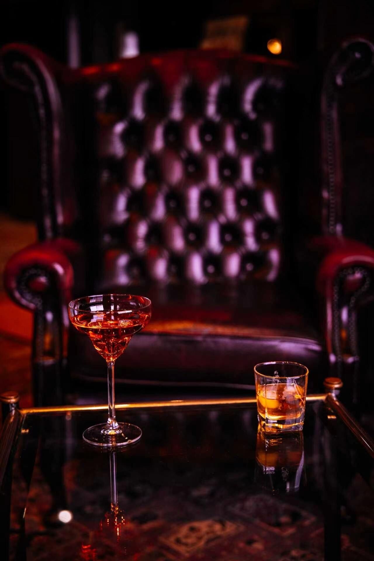 A bar area with a glass of red drink, a shot glass, and a leather chair with a patterned backrest.
