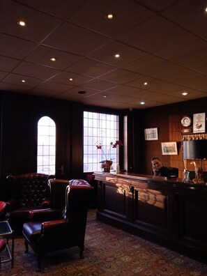 A dimly lit room with a reception desk, leather chairs, a patterned carpet, and a large window with a view. - Hôtel Metropol (Calais)