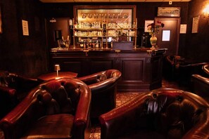 A bar area with leather chairs, a bar counter with bottles, and a sign for Heineken. - Hôtel Metropol (Calais)