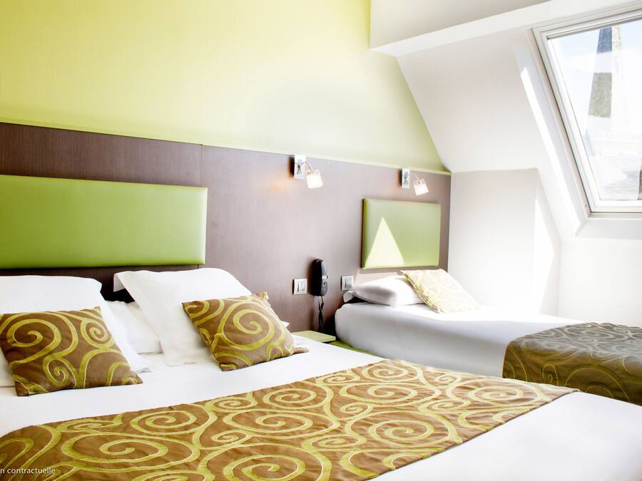 A hotel room with two beds, a green headboard, a window, and a wall-mounted phone.