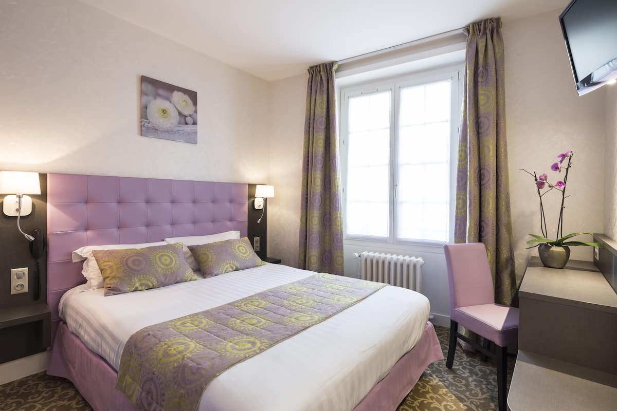 A hotel room with a large bed, a chair, a desk, a TV, and a window with curtains.
