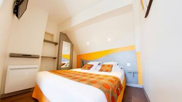 A hotel room with a bed, a radiator, a mirror, and a wall-mounted shelf.