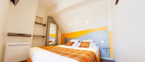 Une chambre d’hôtel avec un lit, un radiateur, un miroir et une étagère fixée au mur.