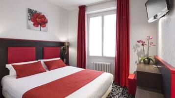 A hotel room with a bed, red curtains, a TV, a plant, and a radiator.