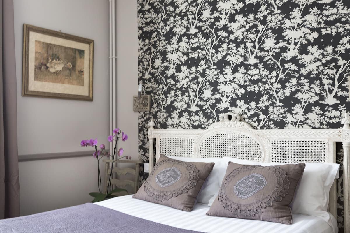 A bedroom with a white bed, a floral wallpaper, and a framed picture on the wall.