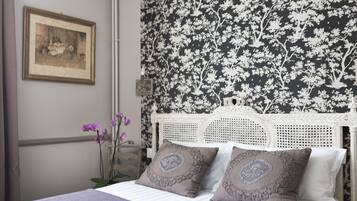 A bedroom with a white bed, a floral wallpaper, and a framed picture on the wall.