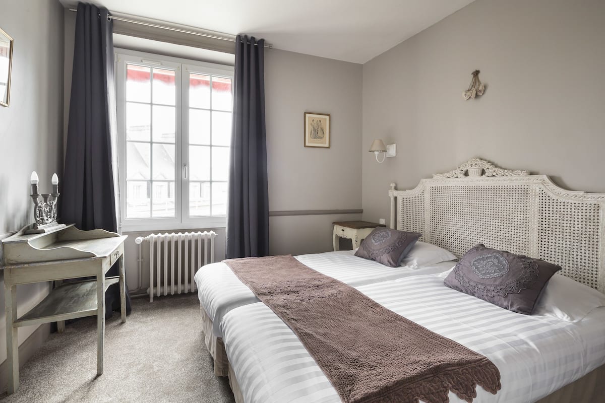 A bedroom with a bed, a desk, a chair, a radiator, and a window with curtains.