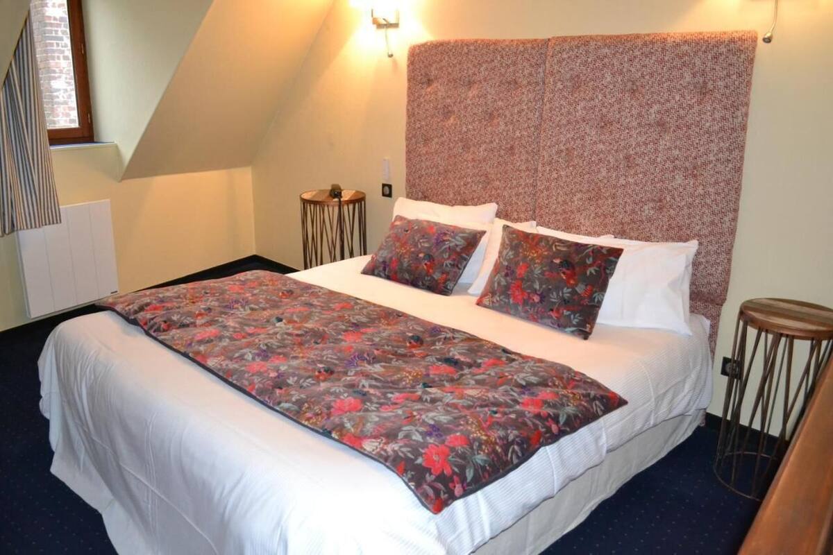 A bedroom with a large bed, a patterned headboard, a small round table, and a window with curtains.