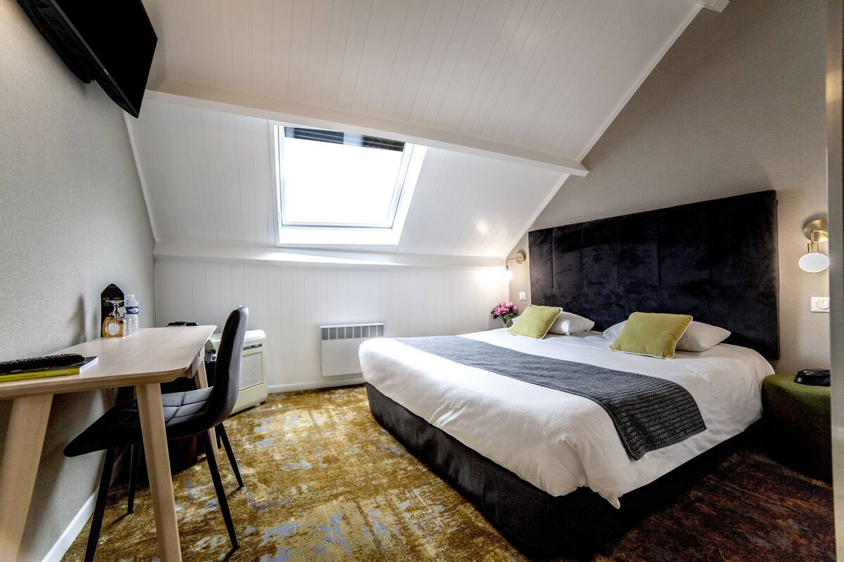 A bedroom with a bed, a desk, and a chair. There is a skylight above the bed.