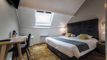 A bedroom with a skylight, a bed with pillows, a desk with a chair, and a radiator.