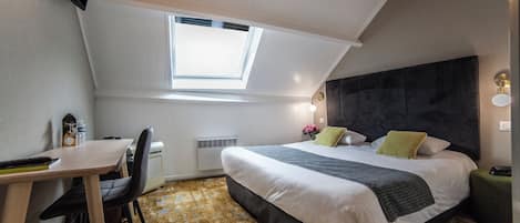 A bedroom with a skylight, a bed with pillows, a desk with a chair, and a radiator.