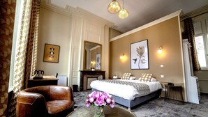 A bedroom with a bed, a chair, a table with a vase of flowers, a fireplace, and wall-mounted lights. - Les Hauts de Montreuil (Montreuil-sur-Mer)