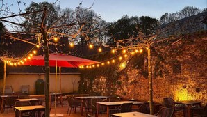 An outdoor patio area with tables and chairs, string lights, and a red umbrella. - Les Hauts de Montreuil (Montreuil-sur-Mer)