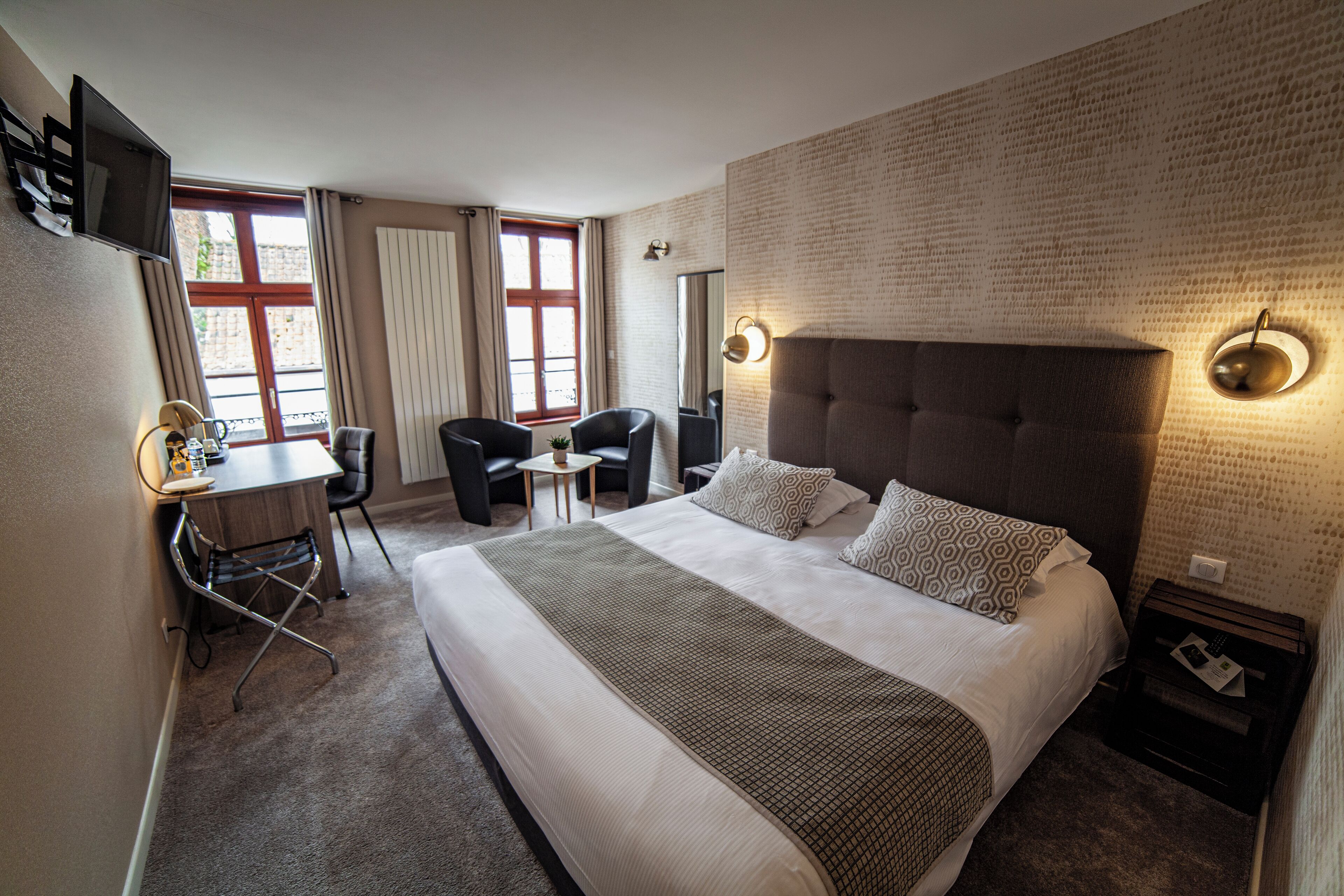 Habitación de hotel con una cama grande, un escritorio con silla, un televisor y un ventanal con cortinas.