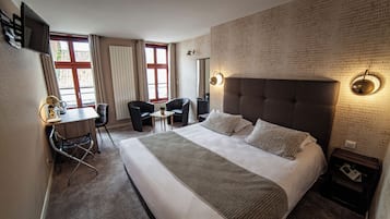 Habitación de hotel con una cama grande, un escritorio con silla, un televisor y un ventanal con cortinas.