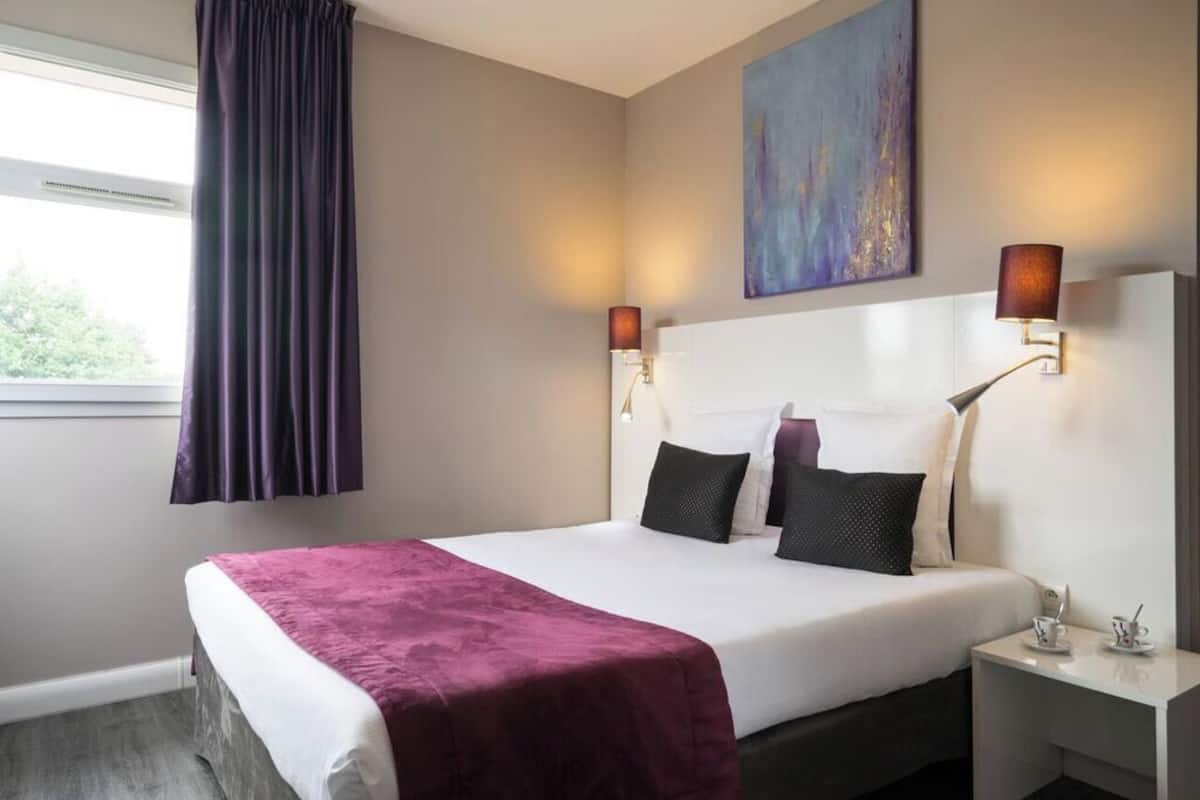 Een hotelkamer met een groot bed, twee bedlampjes, een schilderij aan de muur en een raam met gordijnen.