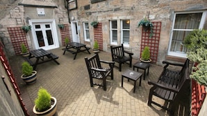 A courtyard with stone walls, wooden benches, and potted plants. - Ambassador Hotel (Glasgow)