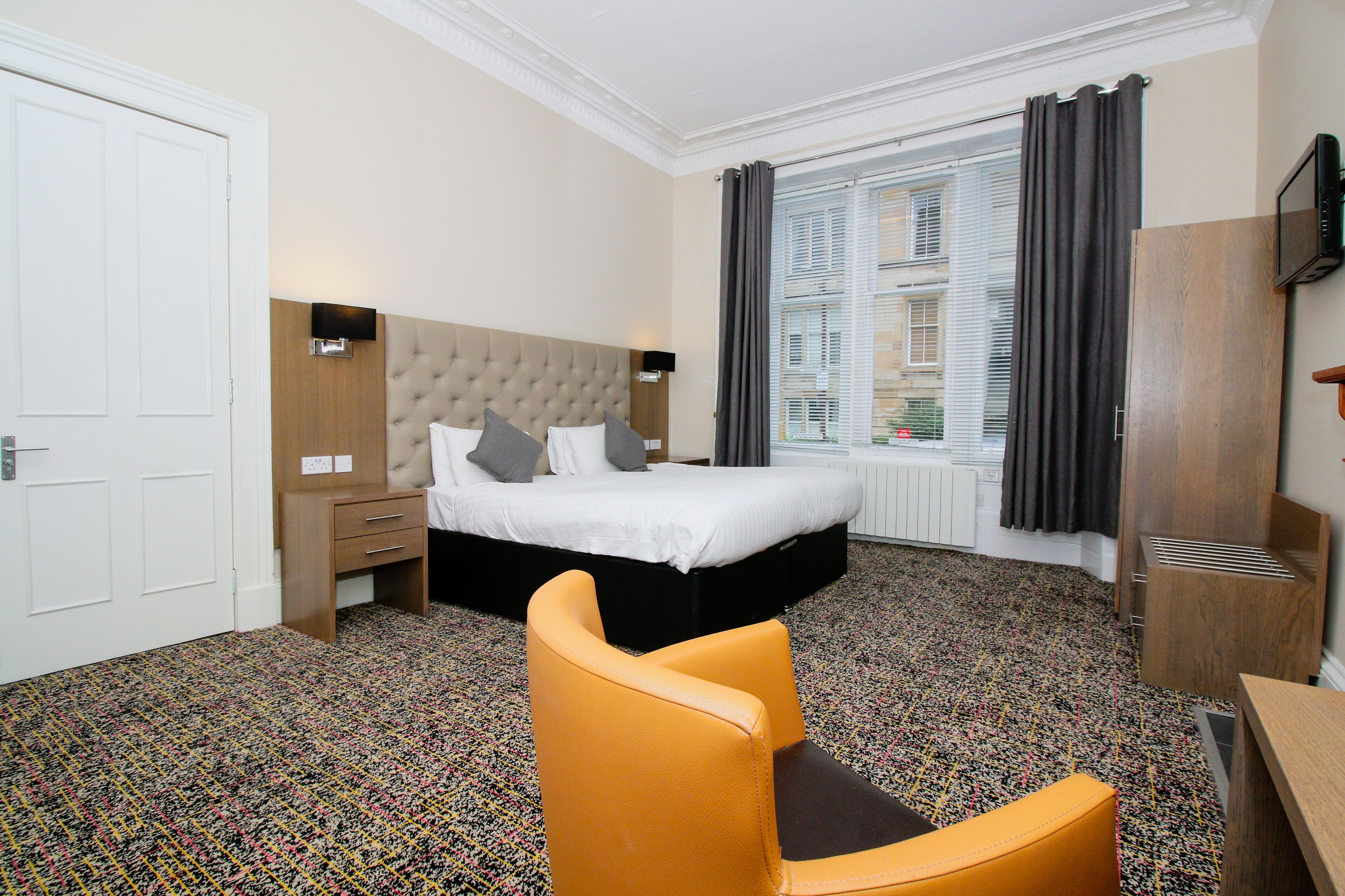A hotel room with a bed, a chair, a desk, and a window with curtains.