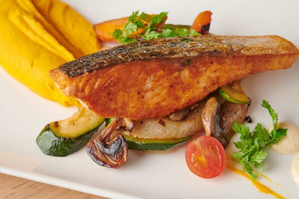 A plate with grilled salmon, vegetables, and a yellow sauce.
