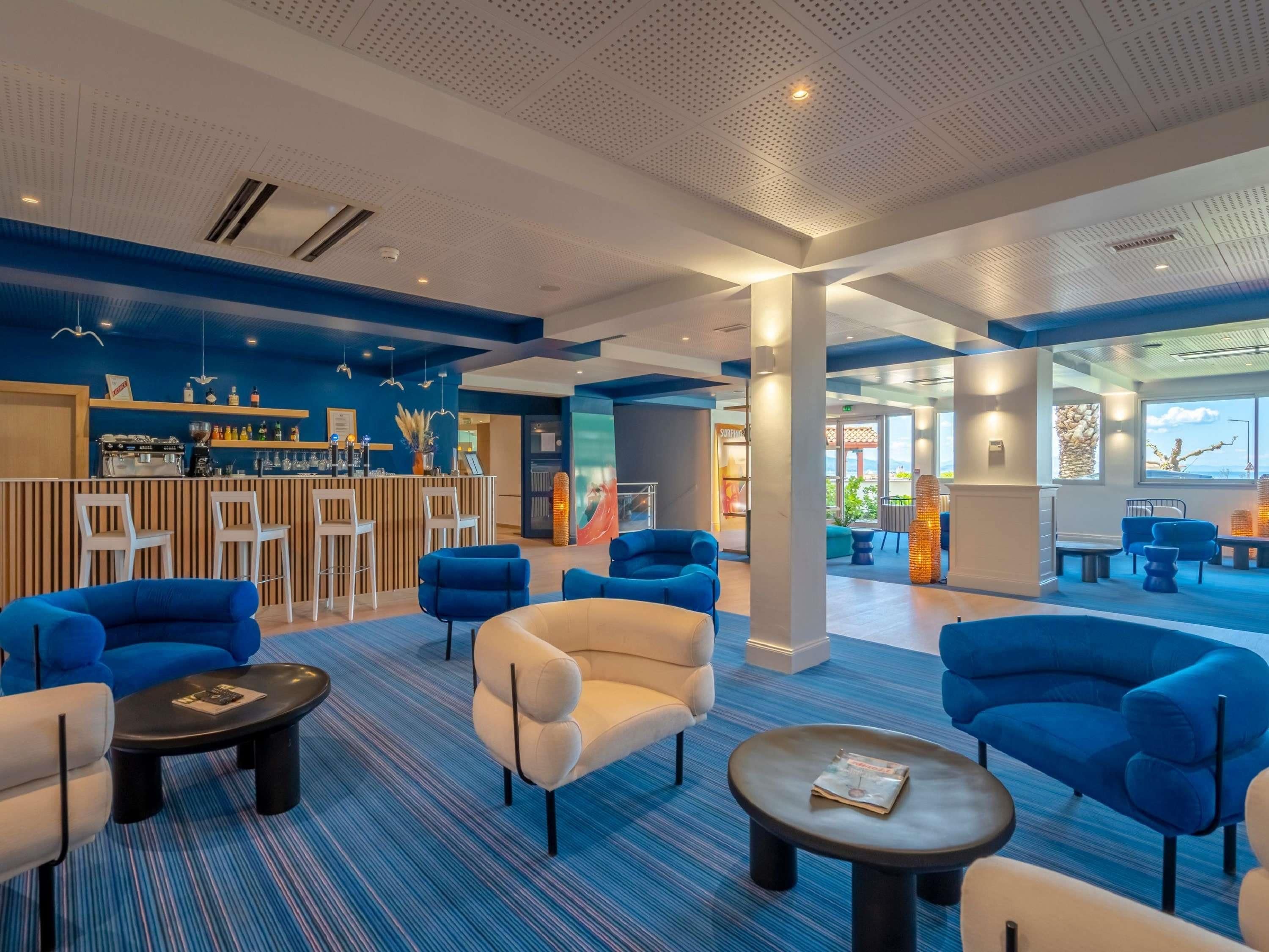 A modern lounge area with blue and white furniture, a bar, and a view of the outdoors.