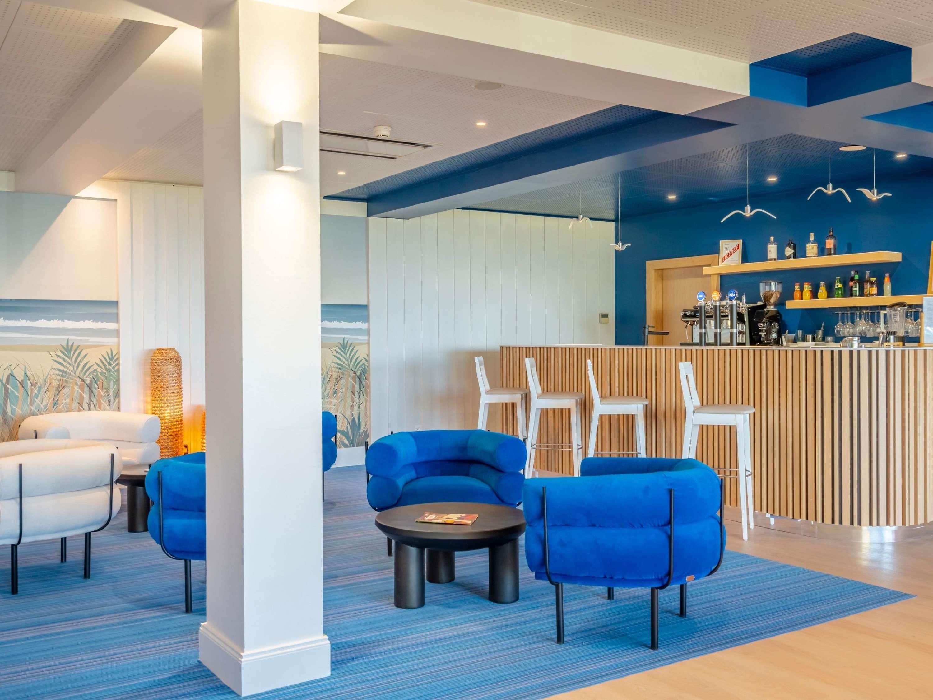 Un área de descanso moderna con asientos azules, una barra y un mural con una escena de playa.