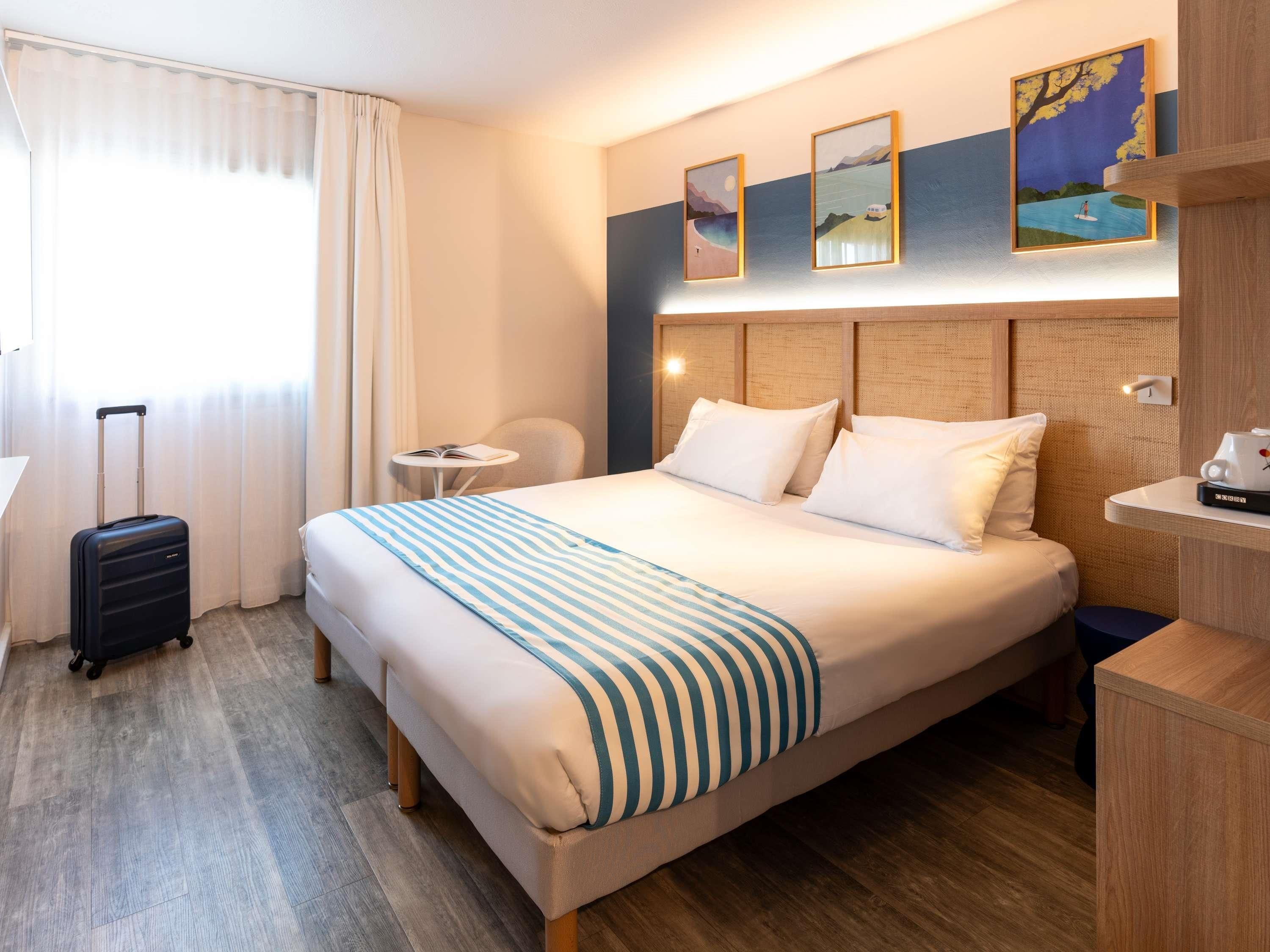 A hotel room with a bed, a suitcase, a small table, and a chair.