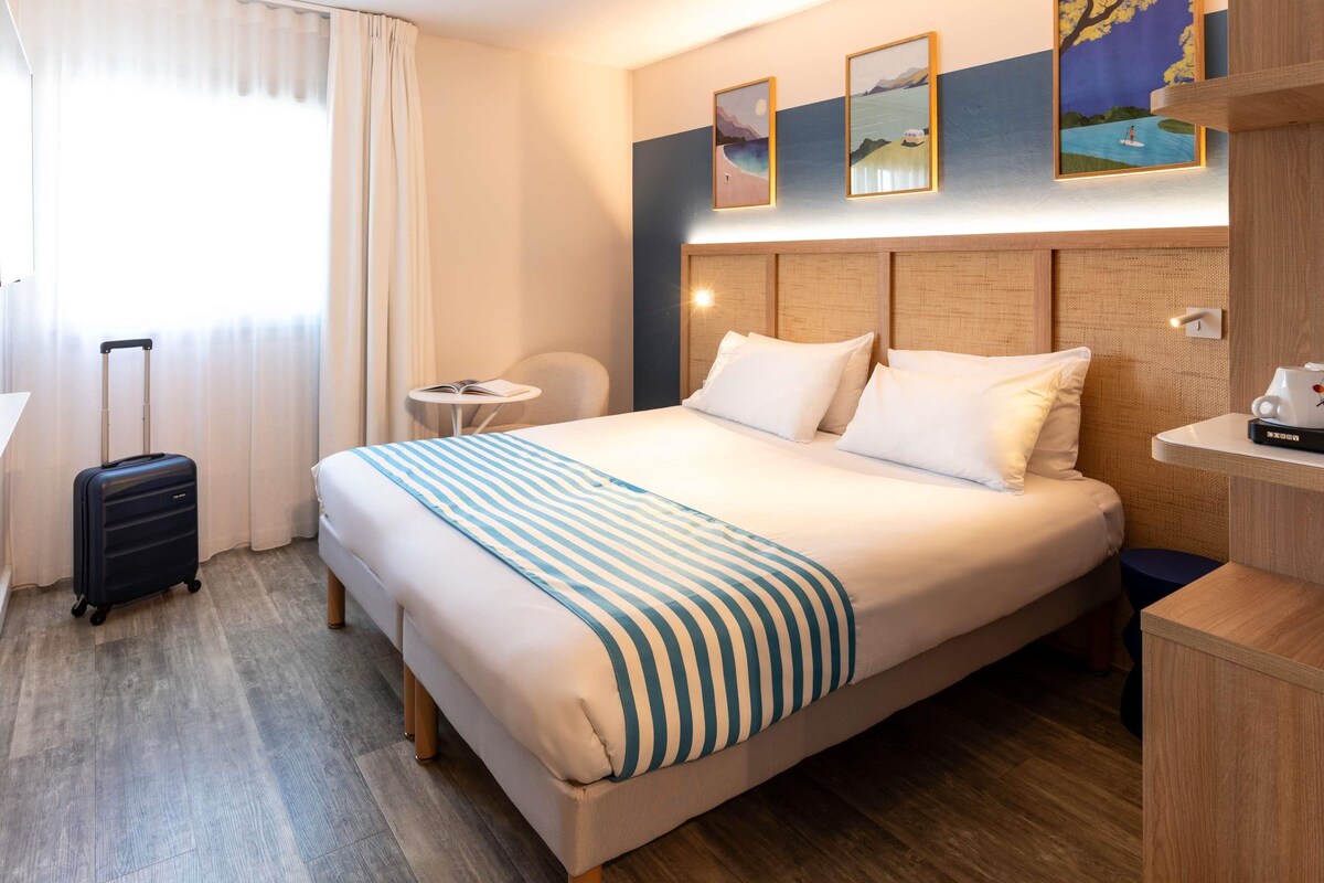 Une chambre d’hôtel avec un lit, une valise, une petite table et une chaise.