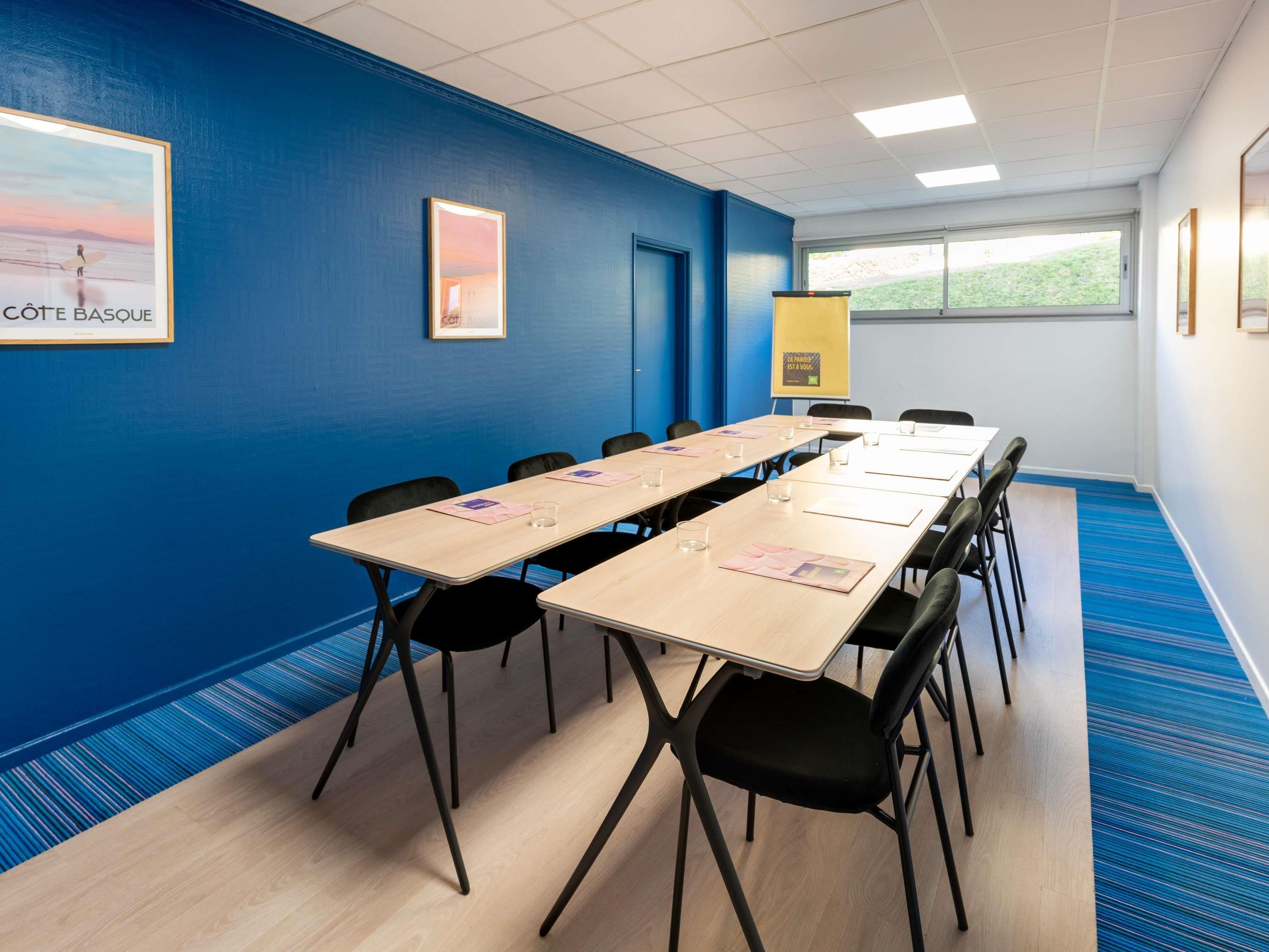 Un salón de conferencias con paredes azules, una mesa larga y sillas negras.