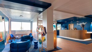 A modern reception area with a blue and white color scheme, a reception desk, and a large window providing natural light. - ibis Styles Biarritz Plage (Ouverture mai 2024) (Biarritz)