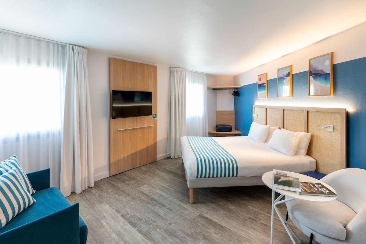 Una habitación de hotel moderna con cama, escritorio, silla, televisor y obras de arte en la pared.
