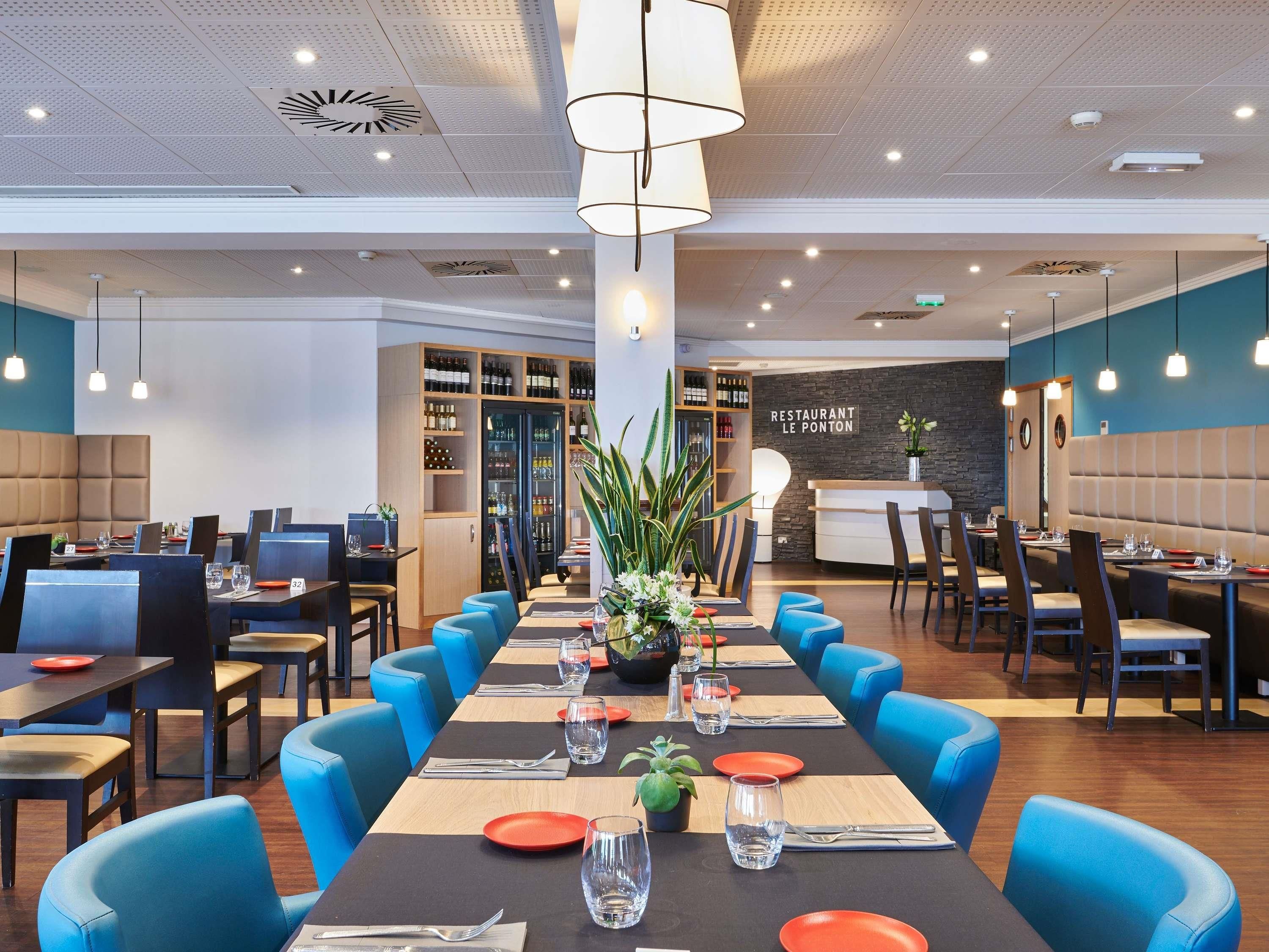A restaurant with long tables, blue chairs, and a wine cooler.