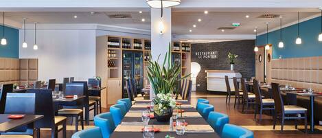A restaurant with long tables, blue chairs, and a wine cooler.