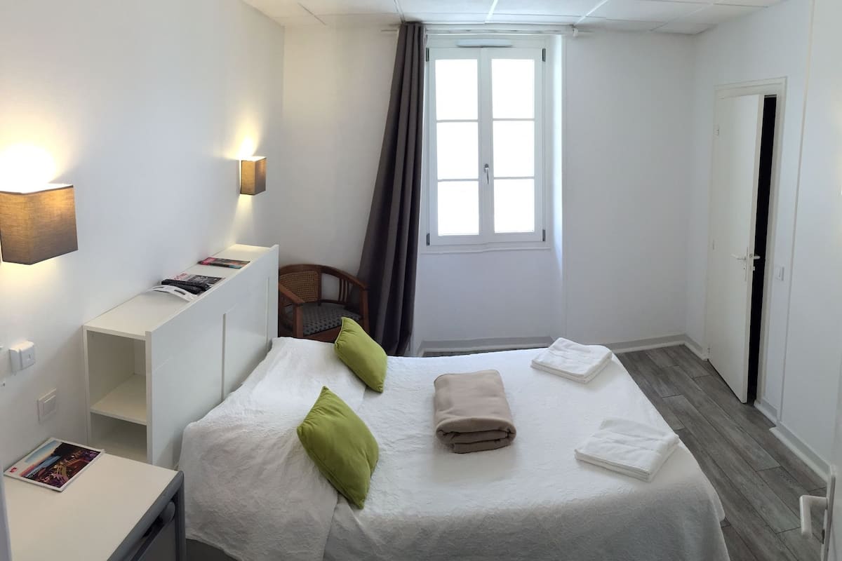 A hotel room with a bed, a desk, a chair, a window with curtains, and a door.