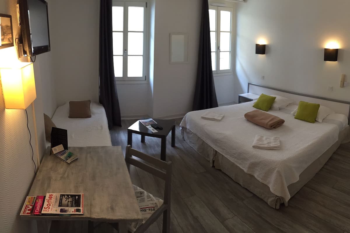 A hotel room with a bed, a desk, a chair, a table, and a TV mounted on the wall.