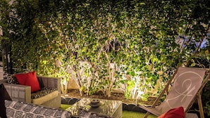 An outdoor seating area with wicker furniture and a glass table, surrounded by lush greenery. - Hôtel des Dunes (La Baule-Escoublac)