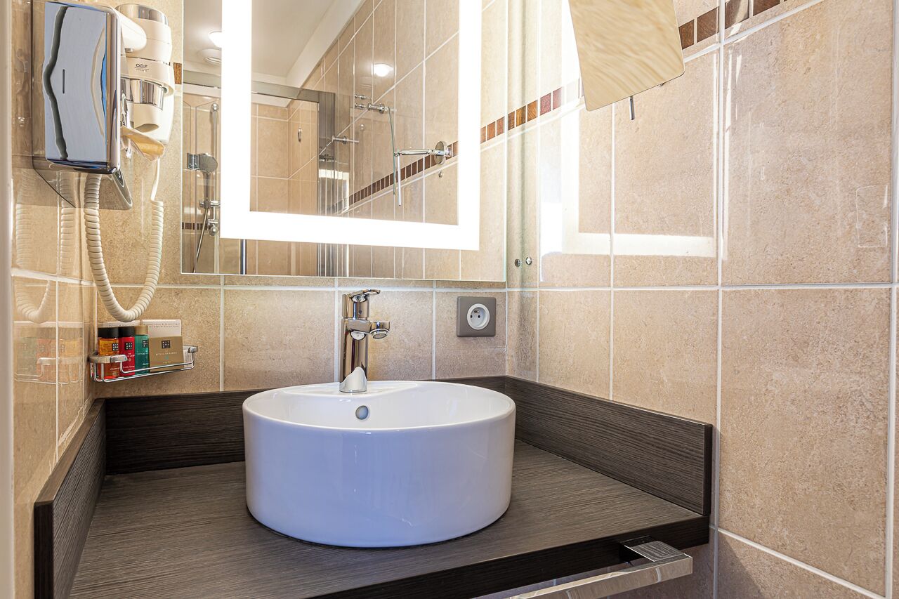 A modern bathroom with a round sink, a mirror, and a hairdryer mounted on the wall.