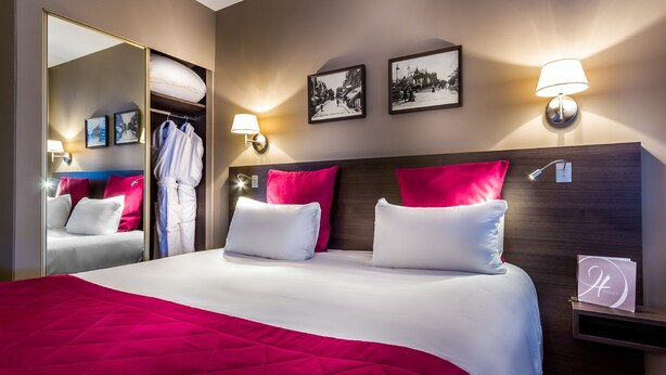 A hotel room with a large bed, red and white bedding, a wooden headboard, two wall-mounted lamps, a mirror, and two framed pictures. - Hôtel des Dunes (La Baule-Escoublac)