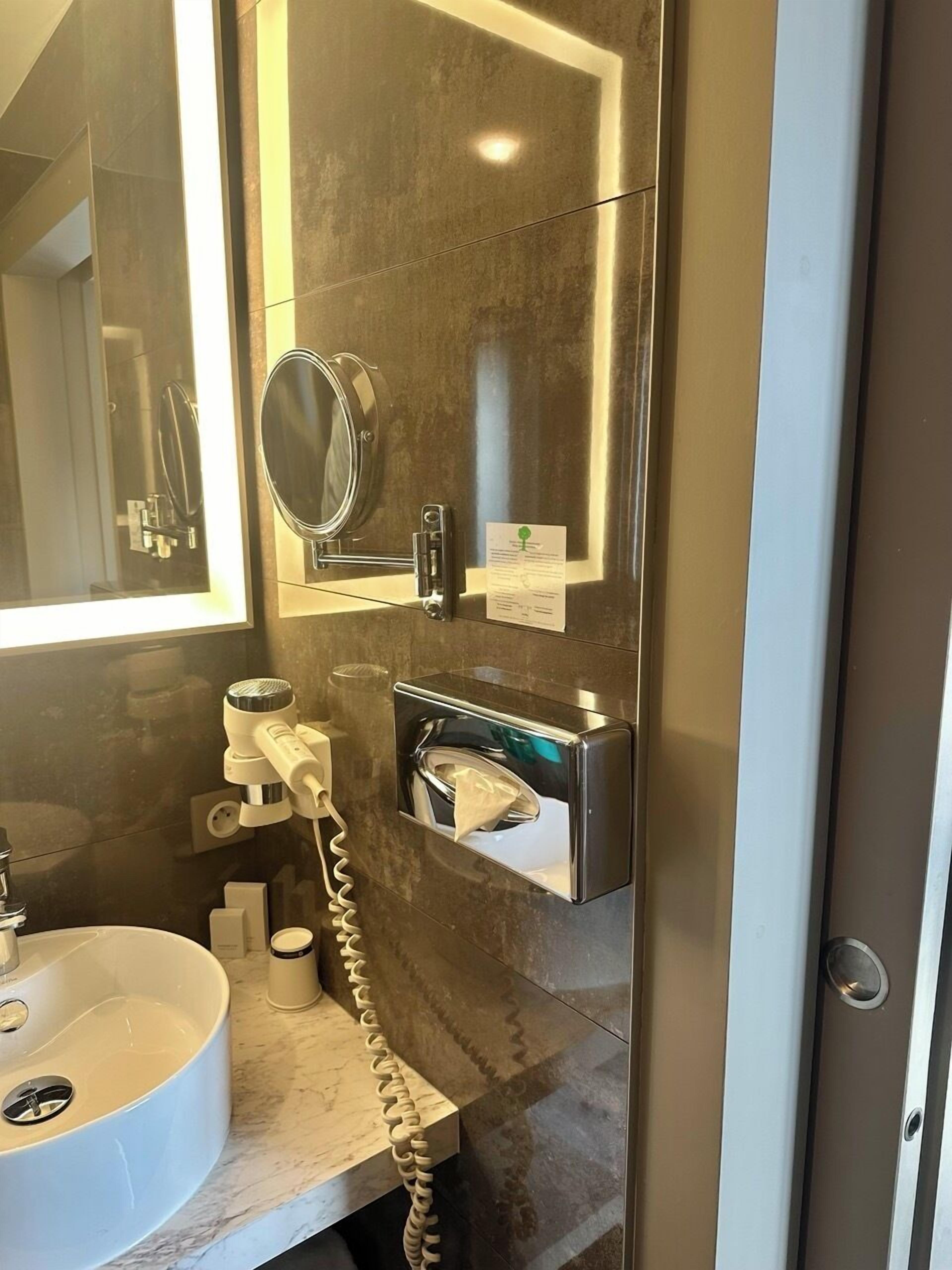 A modern bathroom with a large mirror, a sink, a towel dispenser, and a hand dryer.