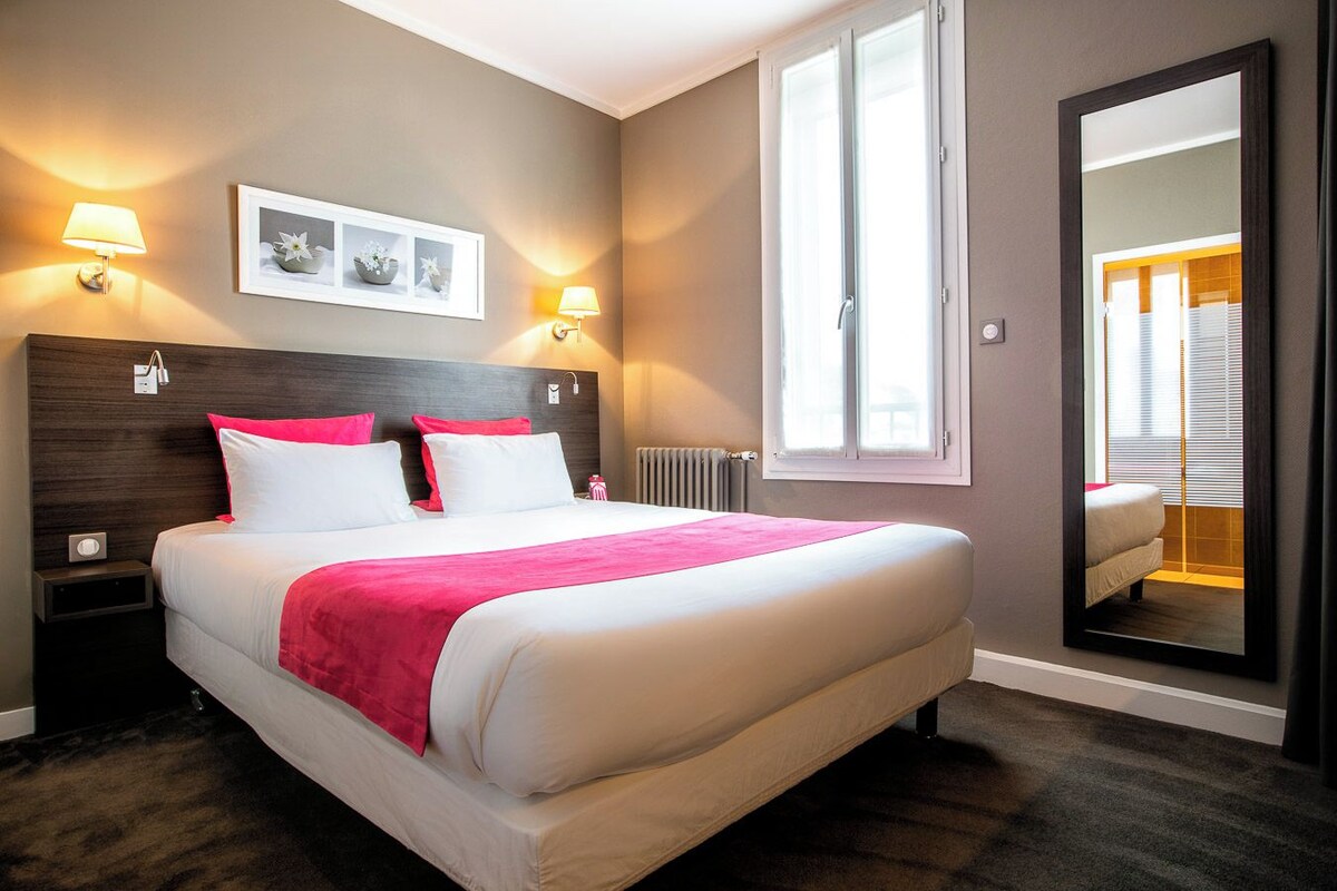 A hotel room with a large bed, two bedside lamps, a window, and a mirror.